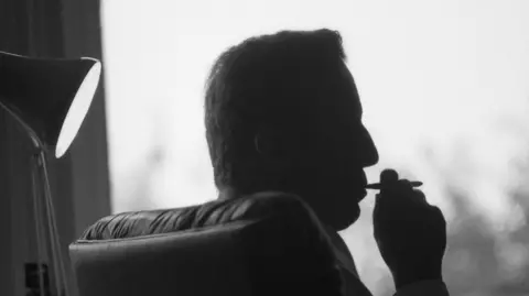Getty Images Frederick Forsyth is shown in silhouette while smoking.