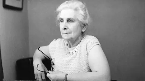 BBC A black and white woman of a woman with light hair and a light top, holding some glasses