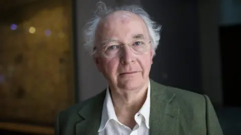 Getty Images Sir Philip Pullman has wispy white hair and a bald crown. He is wearing a green blazer over a white shirt.