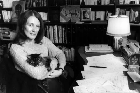 Gamma-Rapho via Getty Images Anne Ernaux at home with a cat, sitting at her desk, in 1984