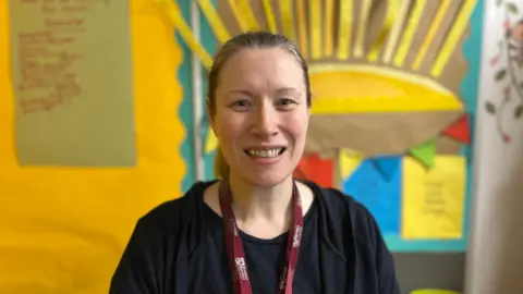 A woman with tied-back hair, wearing a black top, smiles at the camera