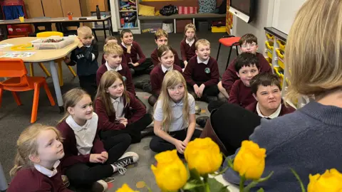 A group of children sit on a classroom floor