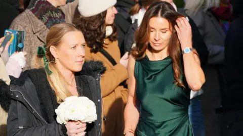 PA Media Holly's mother Ramsay was pictured entering the venue in a floor length emerald green gown. She is touching her brown hair with her hand. A woman to her left is pictured holding a bouquet of flowers.