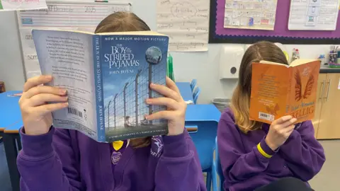 BBC Two schoolgirls hold books up to their faces. You cannot make out what they look like. 