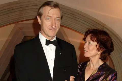 Getty Images On the left is Barnes in a black dinner jacket, black bow tie, white shirt. His wife, Pat Kavanagh, on the right, dressed in burgundy top with stripes, is looking at him, holding his arm