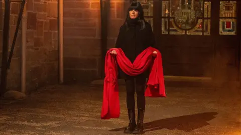 Claudia Winkleman holding the red cloak belonging to the secret traitor